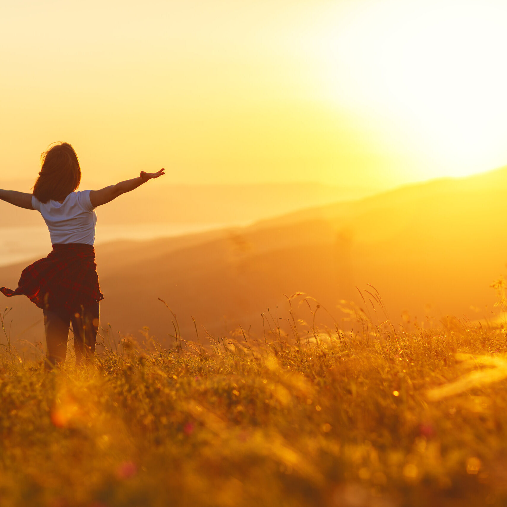 Happy woman standing with her back on the sunset in nature in summer with open hands