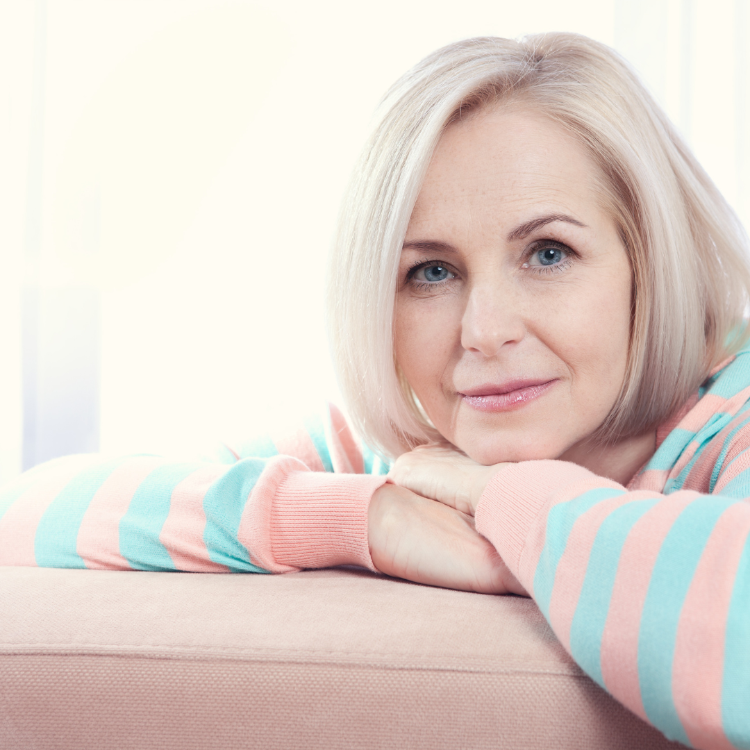 An older woman looking friendly at the camera with hands under chin.